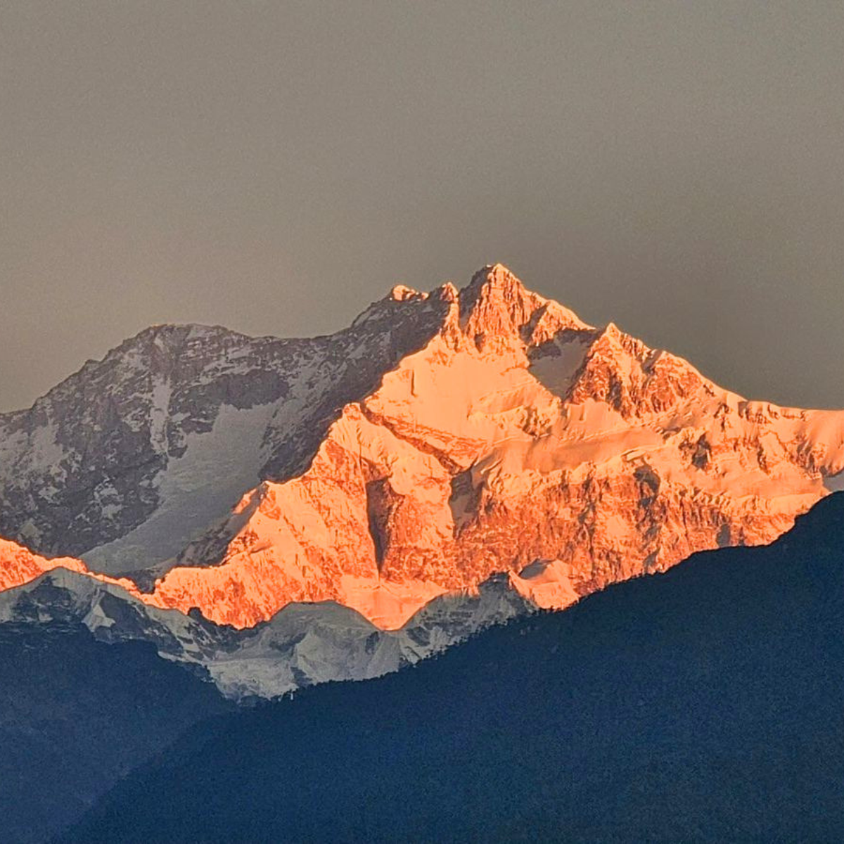Snow-capped mountain peak bathed in warm orange light at sunset.