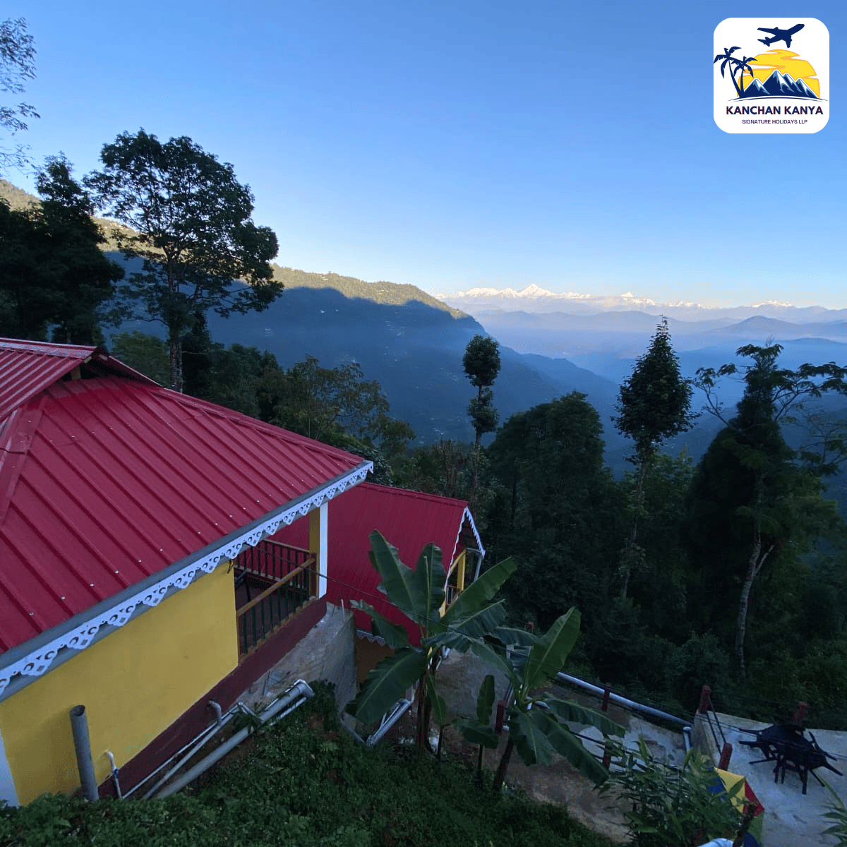 Red-roofed hillside villa with yellow walls, banana plants, and a valley of green hills under a clear blue sky.