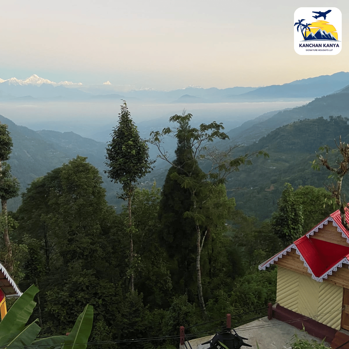 Scenic mountain valley with forested slopes, distant peaks and a red-roofed house in the foreground; KANCHAN KANYA logo in the top-right corner.