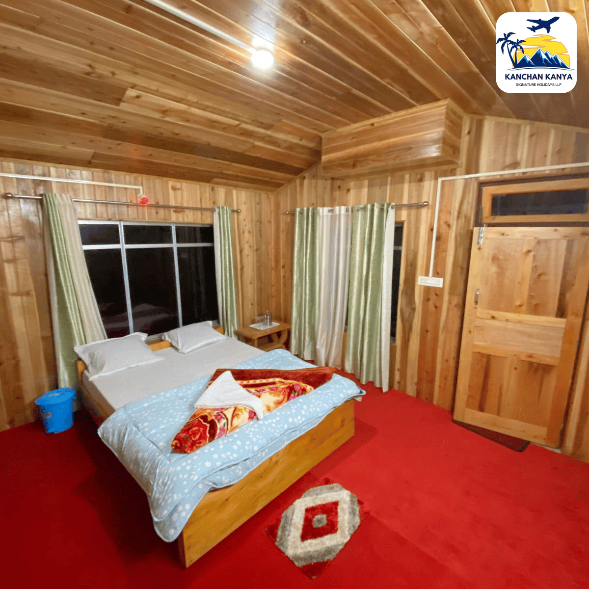 Cozy wooden bedroom with a bed, green curtains, and a red carpet; small nightstand and window on the wall; logo in the top-right corner.