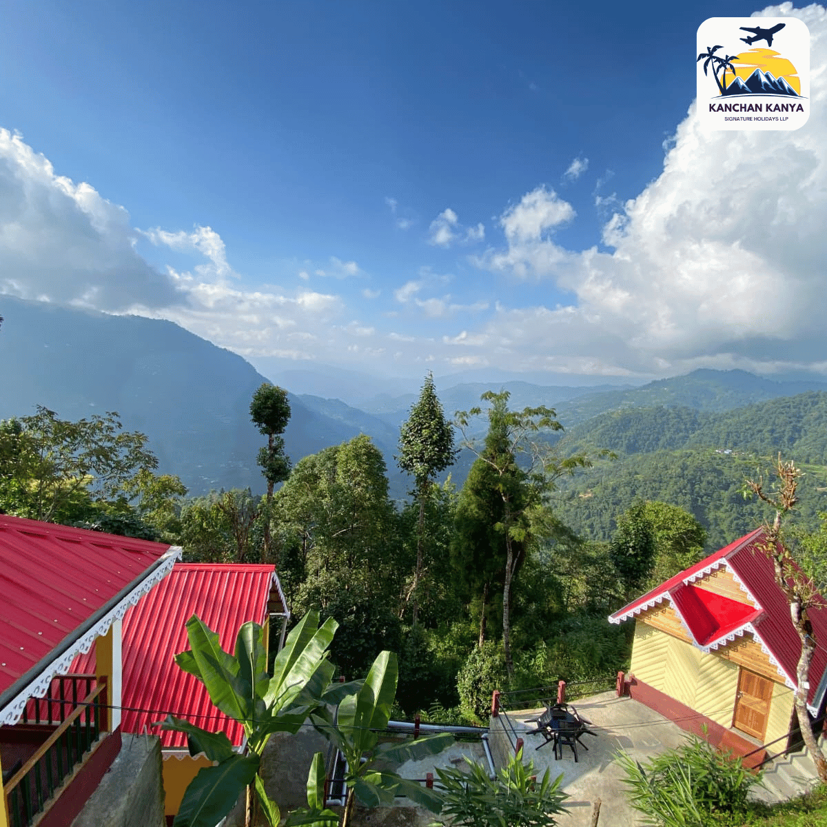 Mountain village with red-roofed houses, lush greenery, and distant blue ridges under a bright sky; logo in the top-right corner.