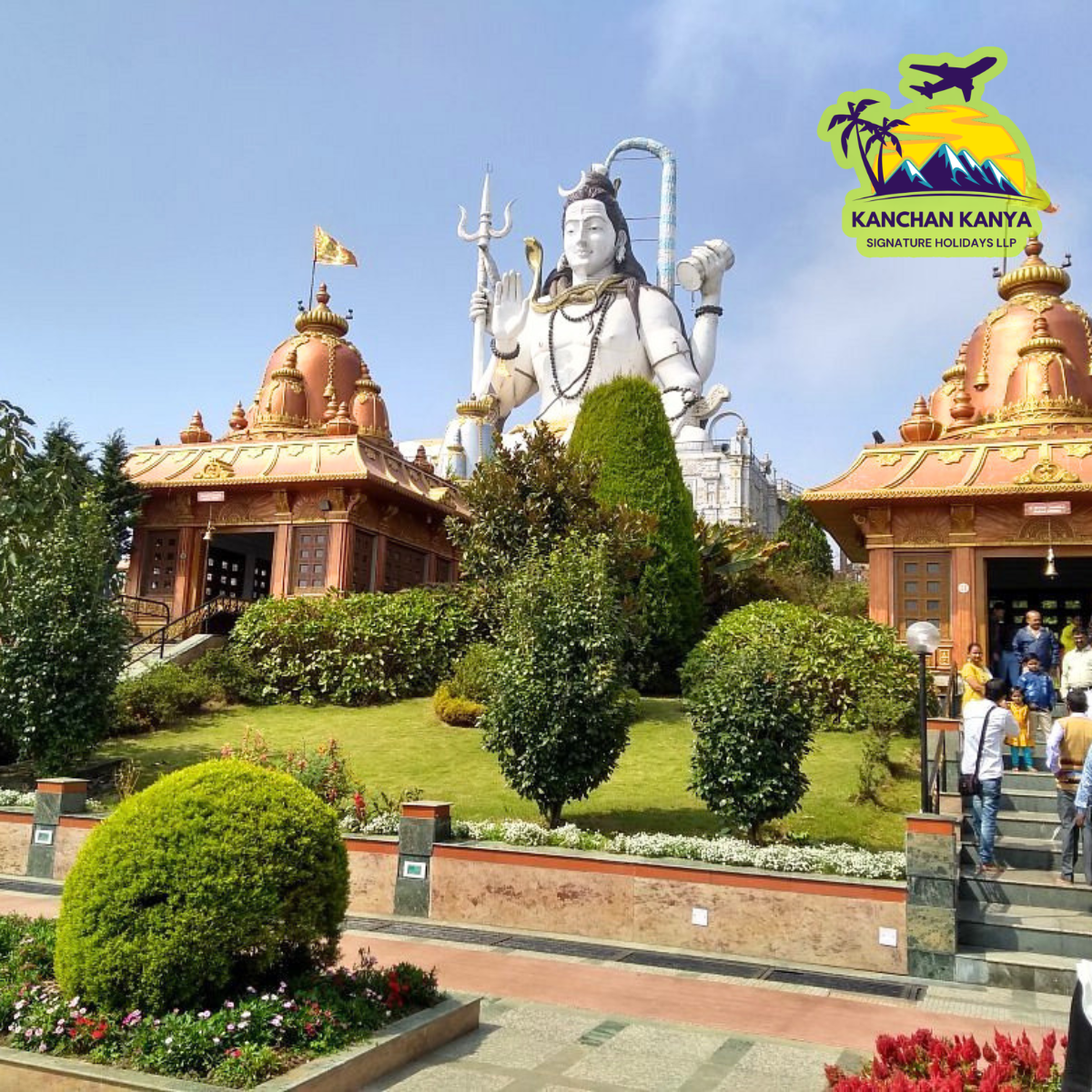 Huge white Shiva statue over a temple complex with orange-roofed pavilions and a neatly manicured garden; visitors walk around.