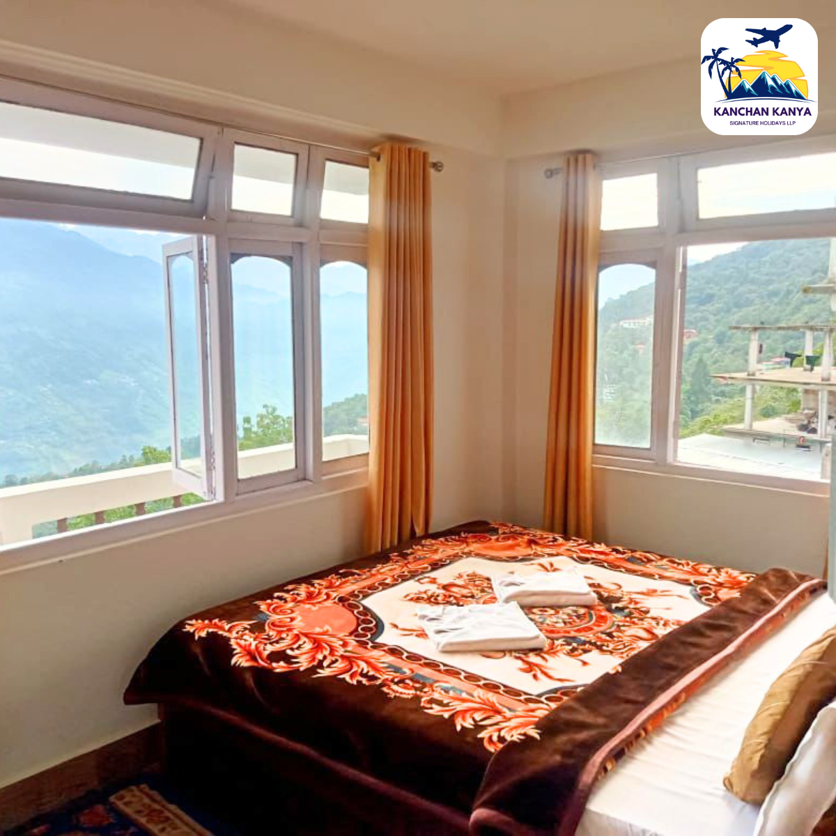 Hotel room with a bed covered by a red floral blanket and large windows offering a mountain view.