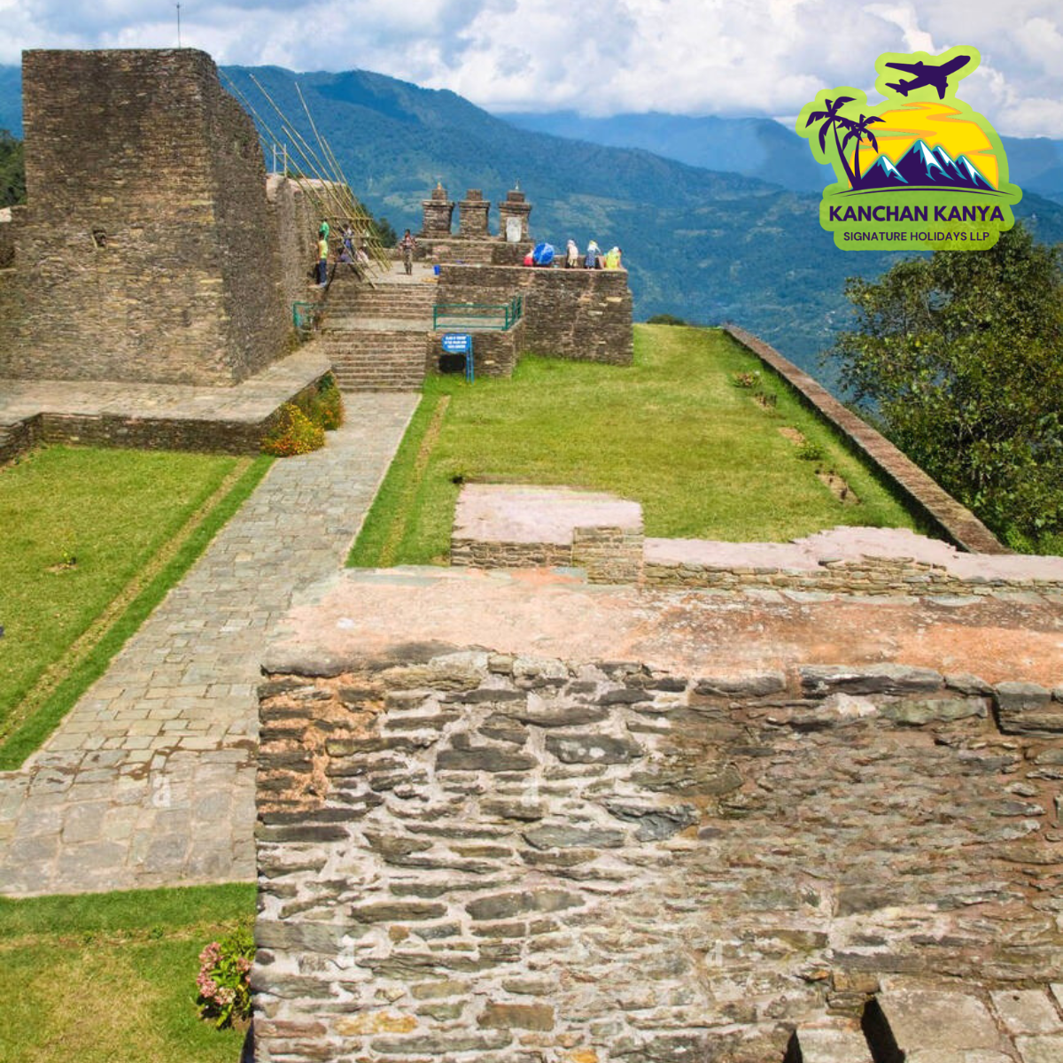 Ancient stone fortress with steps and visitors on a hilltop, overlook of mountains in the distance; travel logo in the top-right corner
