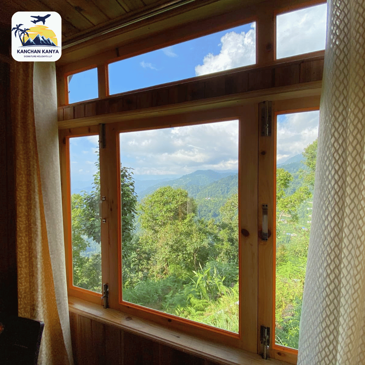 Wood-framed cabin window with a lush mountain and treed view; logo in the top-left corner.