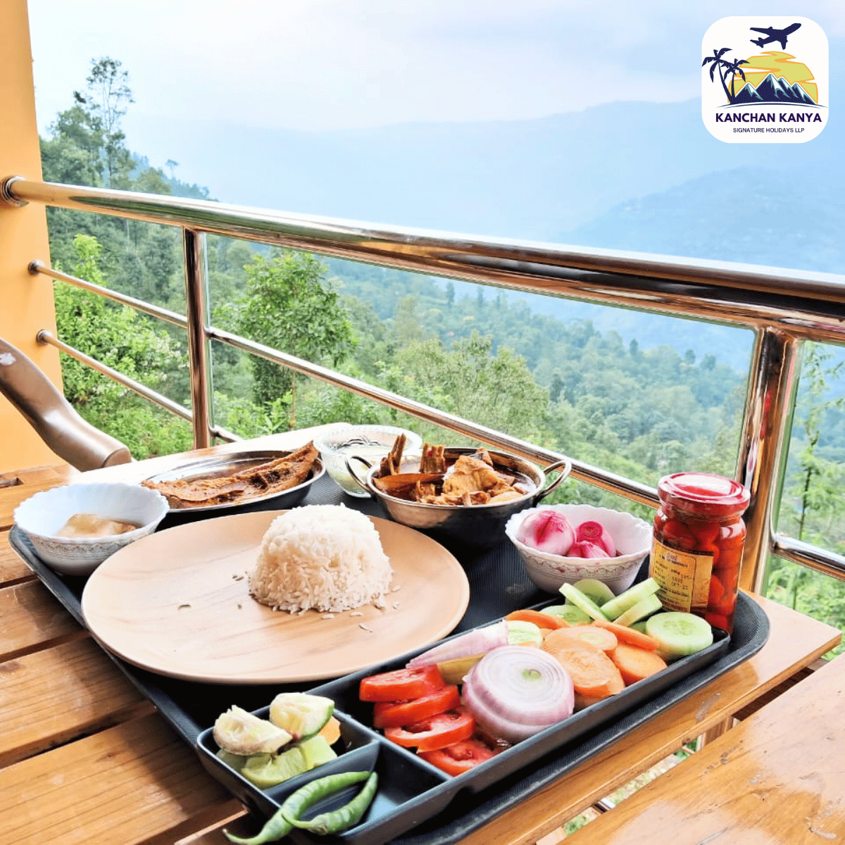 Tray of rice with sides (curry, vegetables, pickles) on a balcony table, overlooking misty mountains; logo in top-right corner—KANCHAN KANYA.
