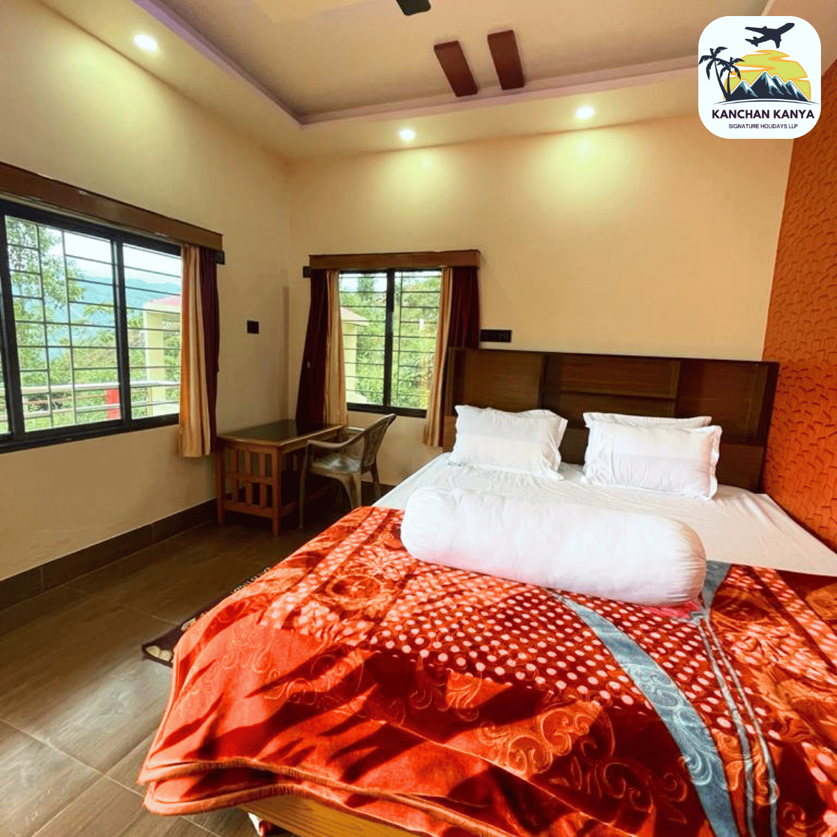 Hotel room with a large bed, white pillows, a red patterned quilt, and a wooden headboard by two windows. Outside greenery visible.