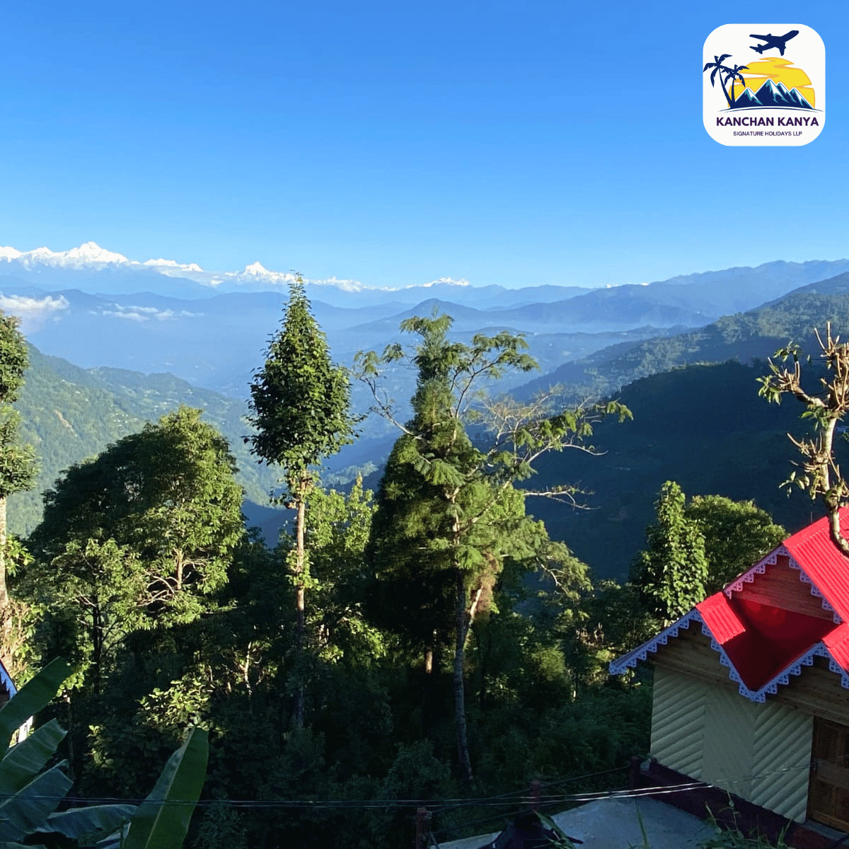 Mountain valley view with green trees and distant blue mountains under a clear blue sky; a red-roofed building appears in the foreground; logo in the top-right reads 'Kanchan Kanya'