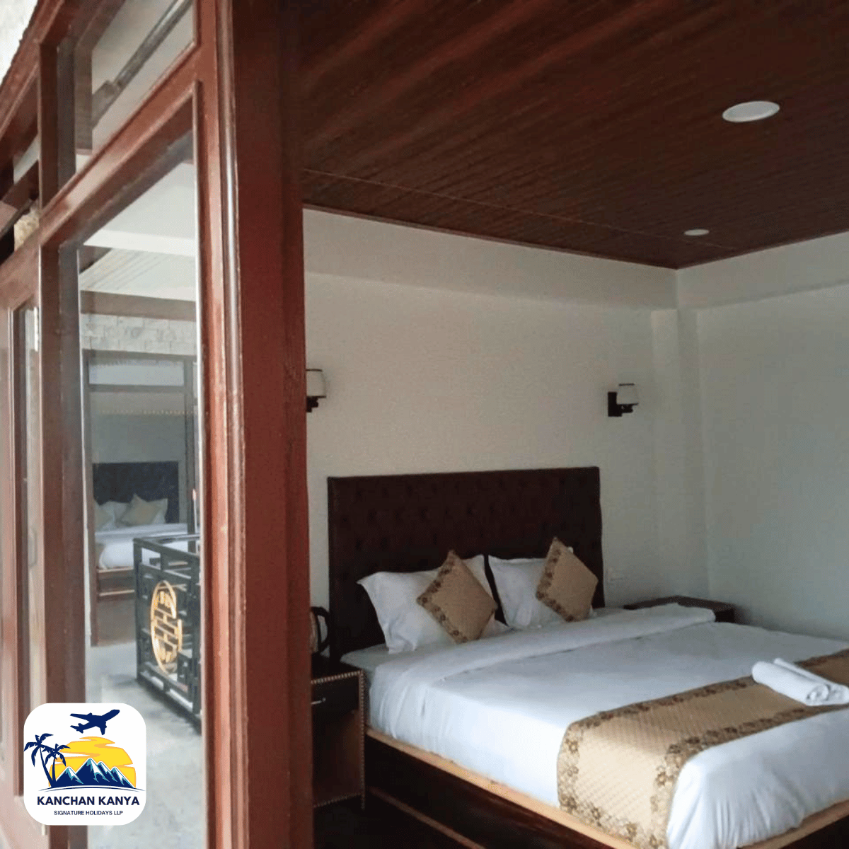10 Hotel room with a king bed, white linens, tan decorative pillows, dark wood headboard, and a wood-paneled ceiling with a doorway to a balcony.