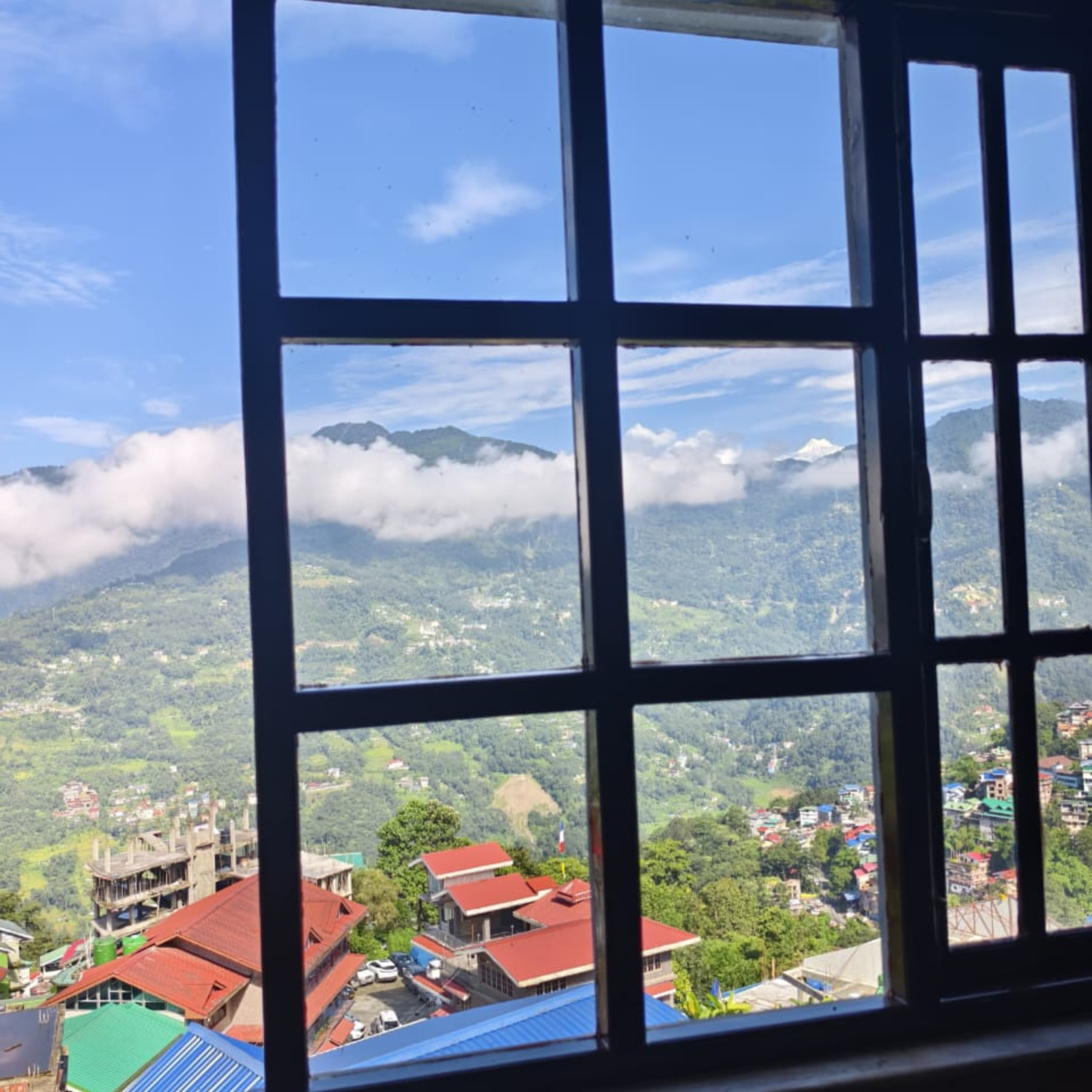Window view of a valley with red-roofed houses, green fields and distant mountains under a blue sky, seen through black window bars