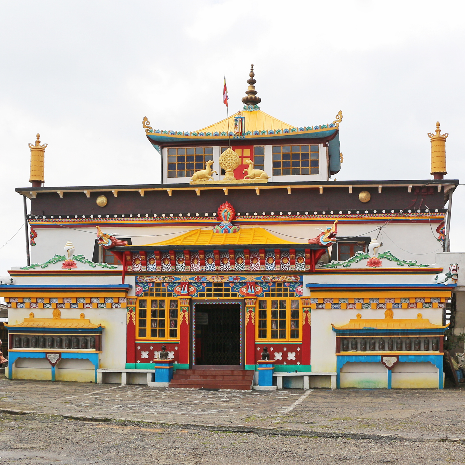 Colorful Buddhist temple facade with a yellow roof, red doors, and gold decorative figures against a cloudy sky.