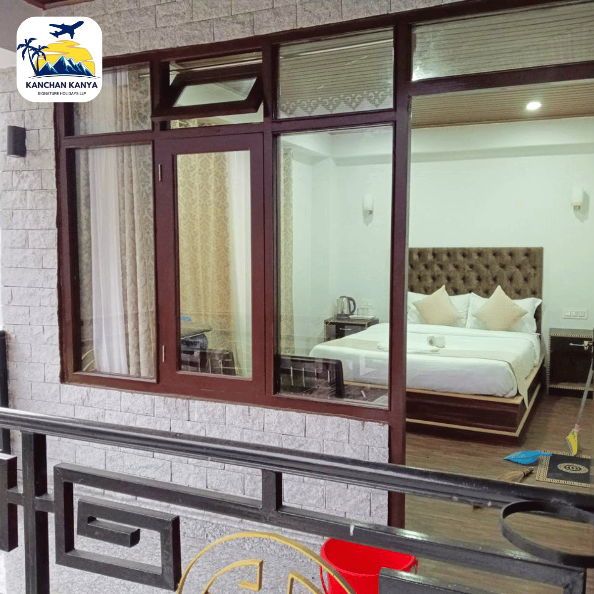 13 Hotel bedroom seen through large glass doors: tufted headboard bed, two nightstands, and a kettle on a side table.