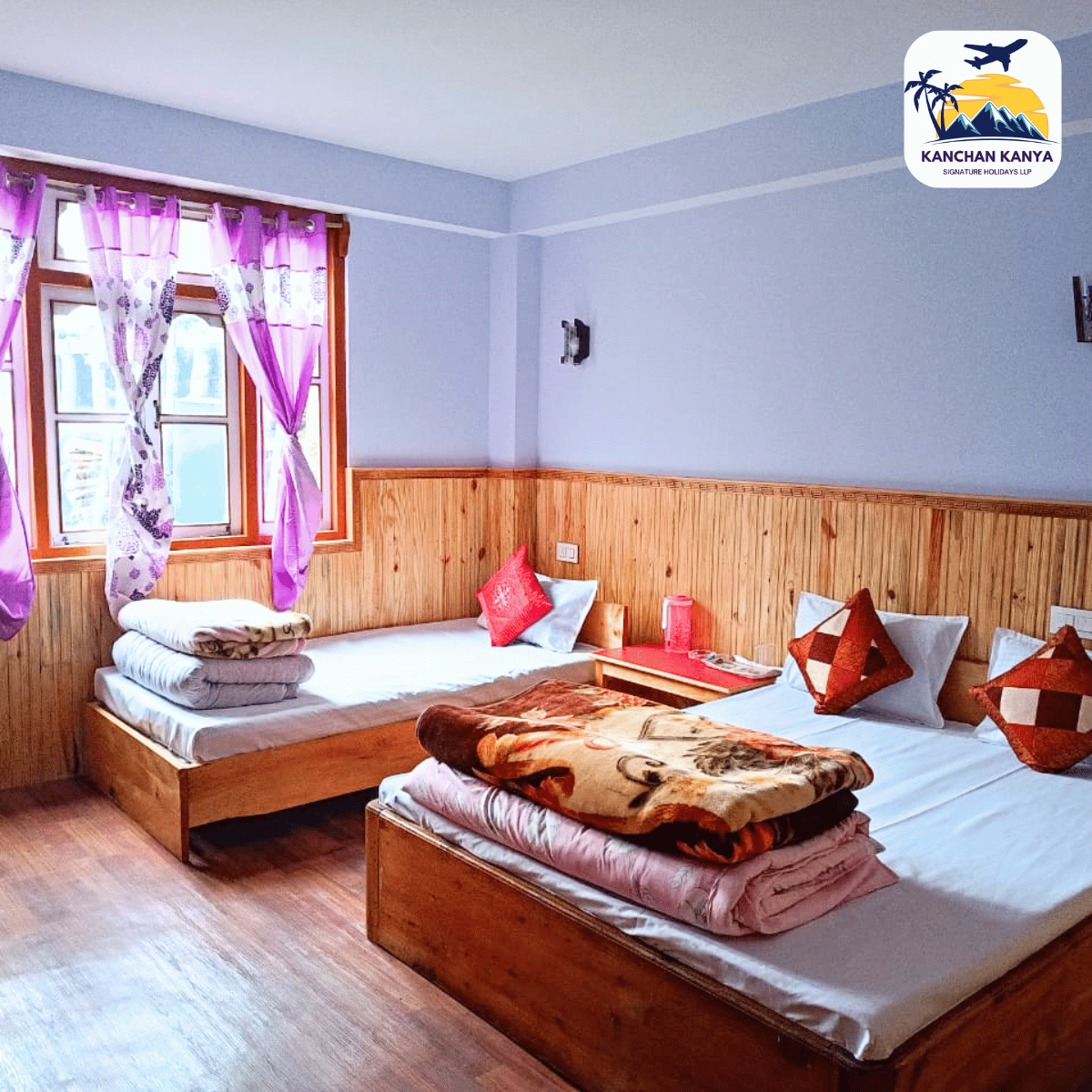 15 A bright hotel room with two wooden-frame beds, purple curtains, and folded blankets stacked at the foot of the beds.