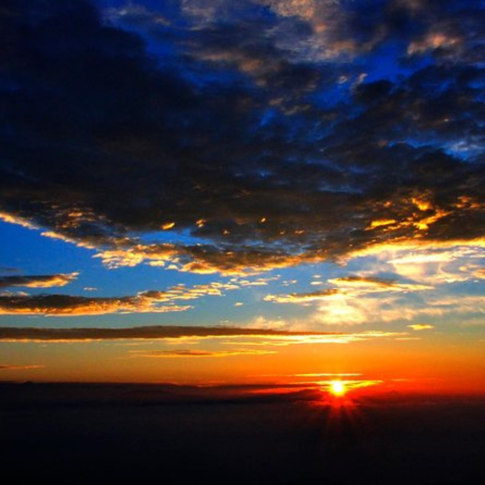 Sunset over a calm ocean with orange sky and dark clouds on the horizon.