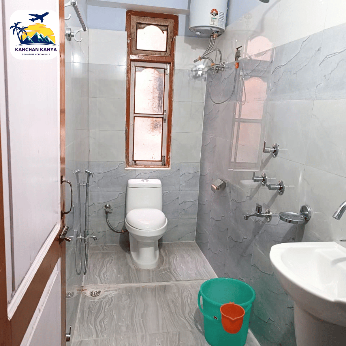 19 Small bathroom with a toilet, shower fixtures, and a green bucket in the foreground; logo on the left wall reads KANCHAN KANYA.