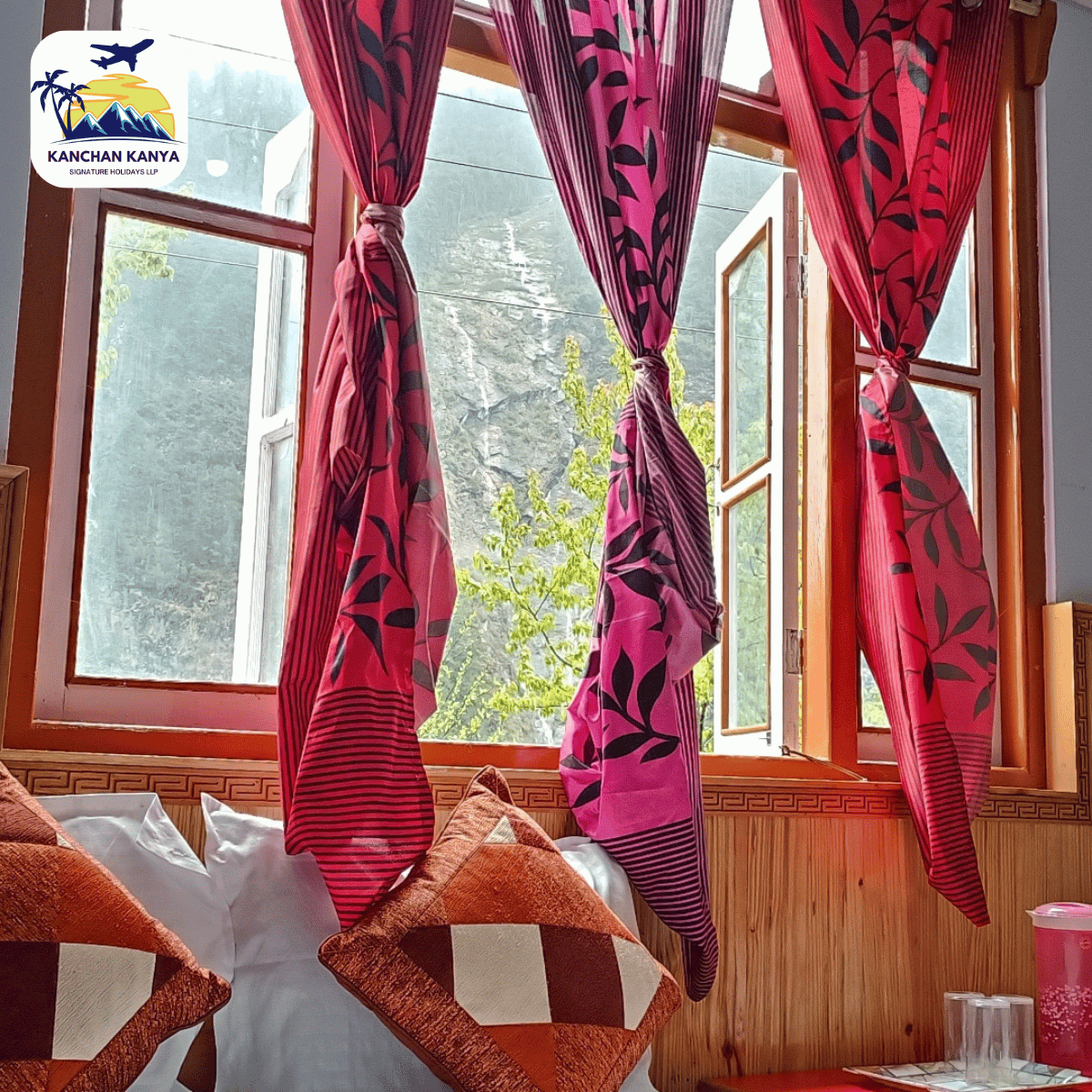 22 Cozy room interior with pink patterned curtains tied back, orange and white patterned cushions on a sofa, and an open window revealing a rocky outdoor scene.