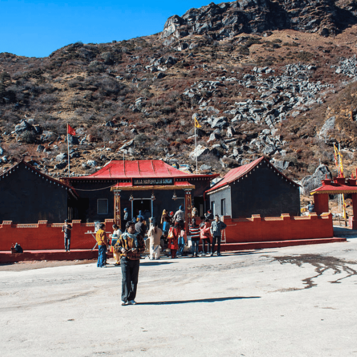 34 Temple complex with red-roofed buildings and a line of people entering the entrance against a rocky hillside.