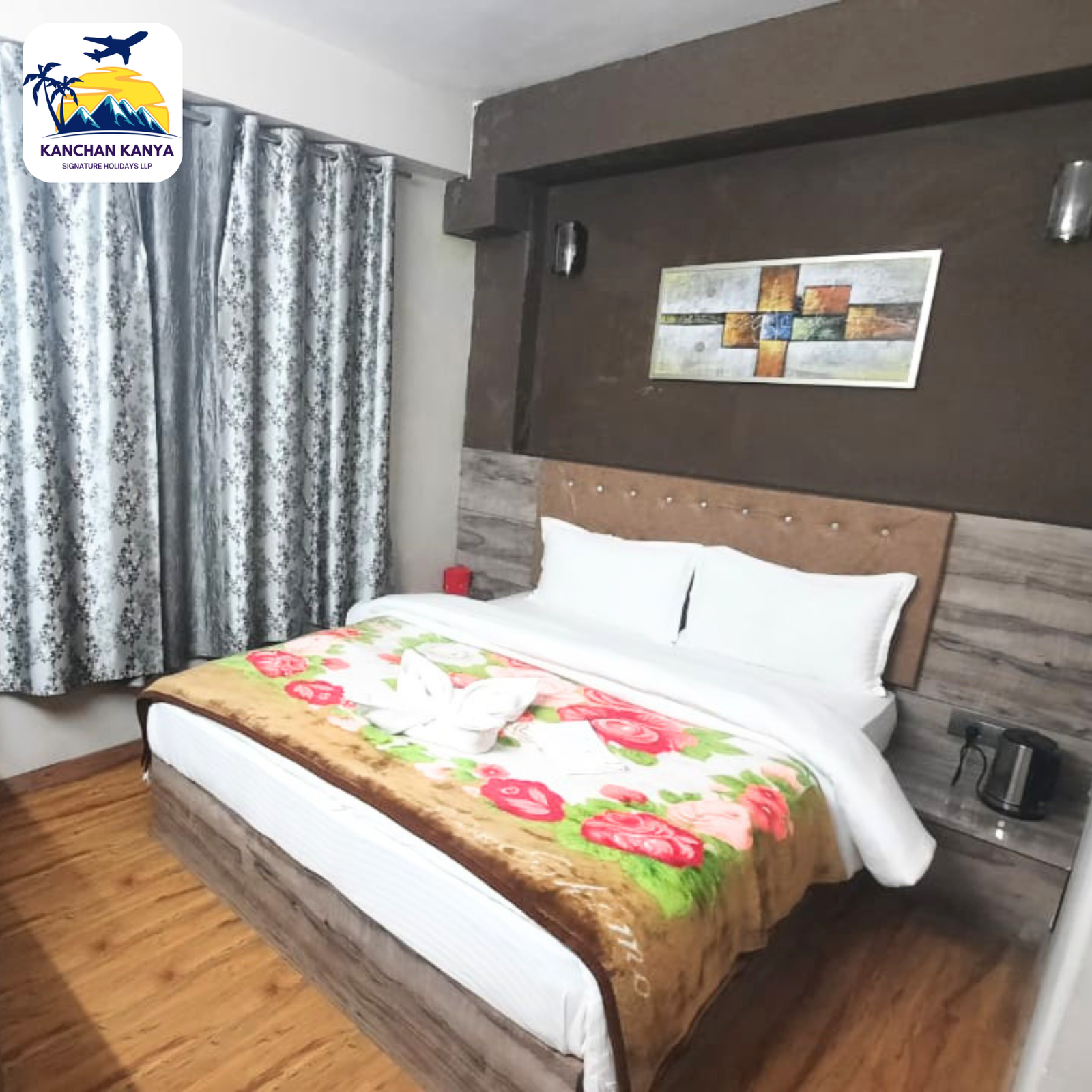 Hotel bedroom with a large bed, white linens, and a floral green-pink bed runner against a dark wooden headboard and patterned curtains in the background.