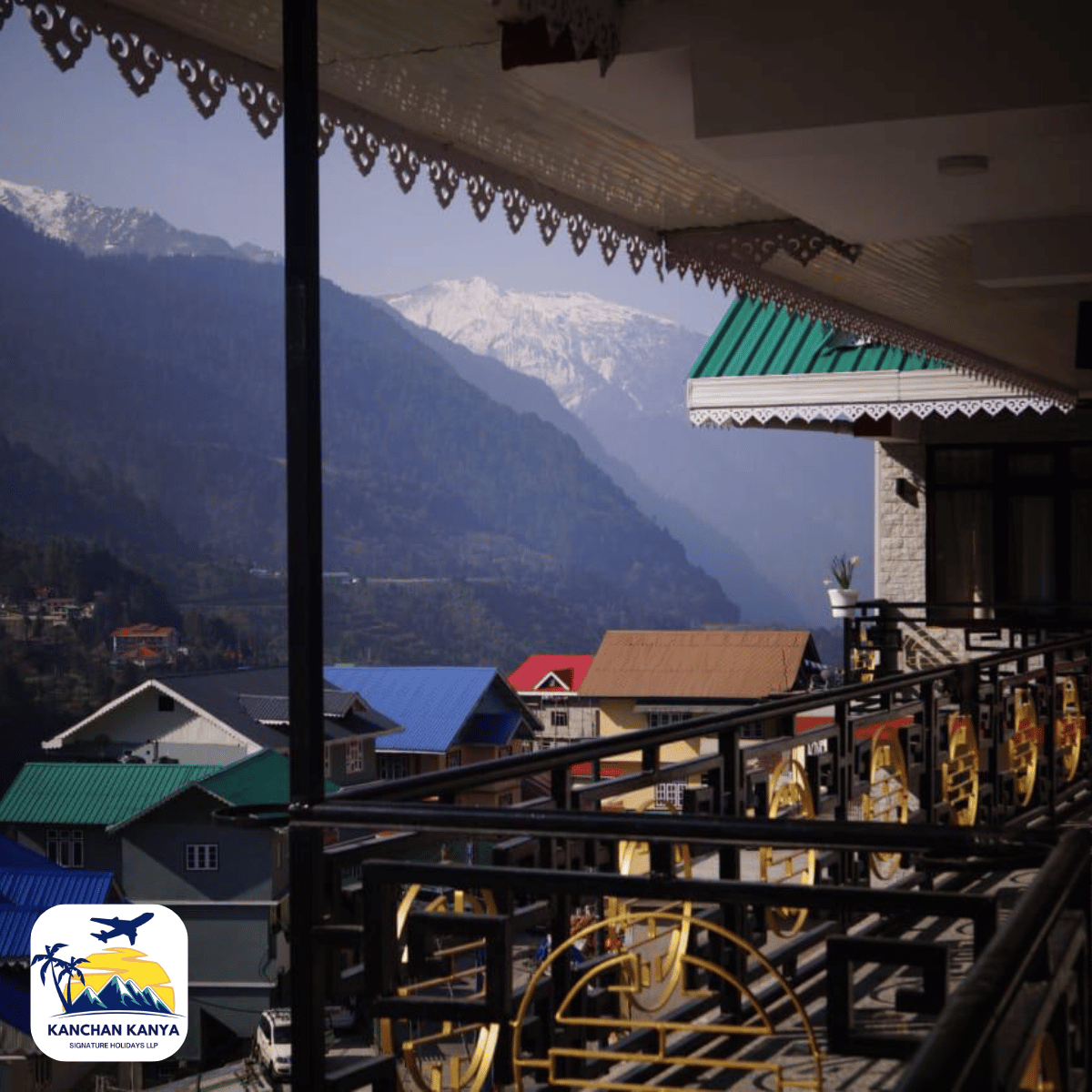 7 Balcony view of a mountainside village with colorful roofs and snow-capped peaks in the background; logo bottom-left.