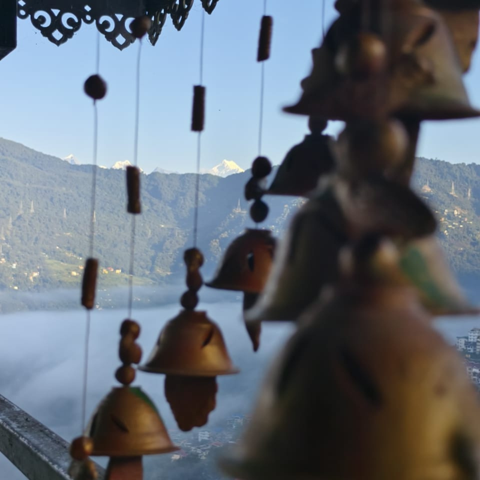 Blurred view of hanging wooden beads and bells with distant mountains and a lake in the background.