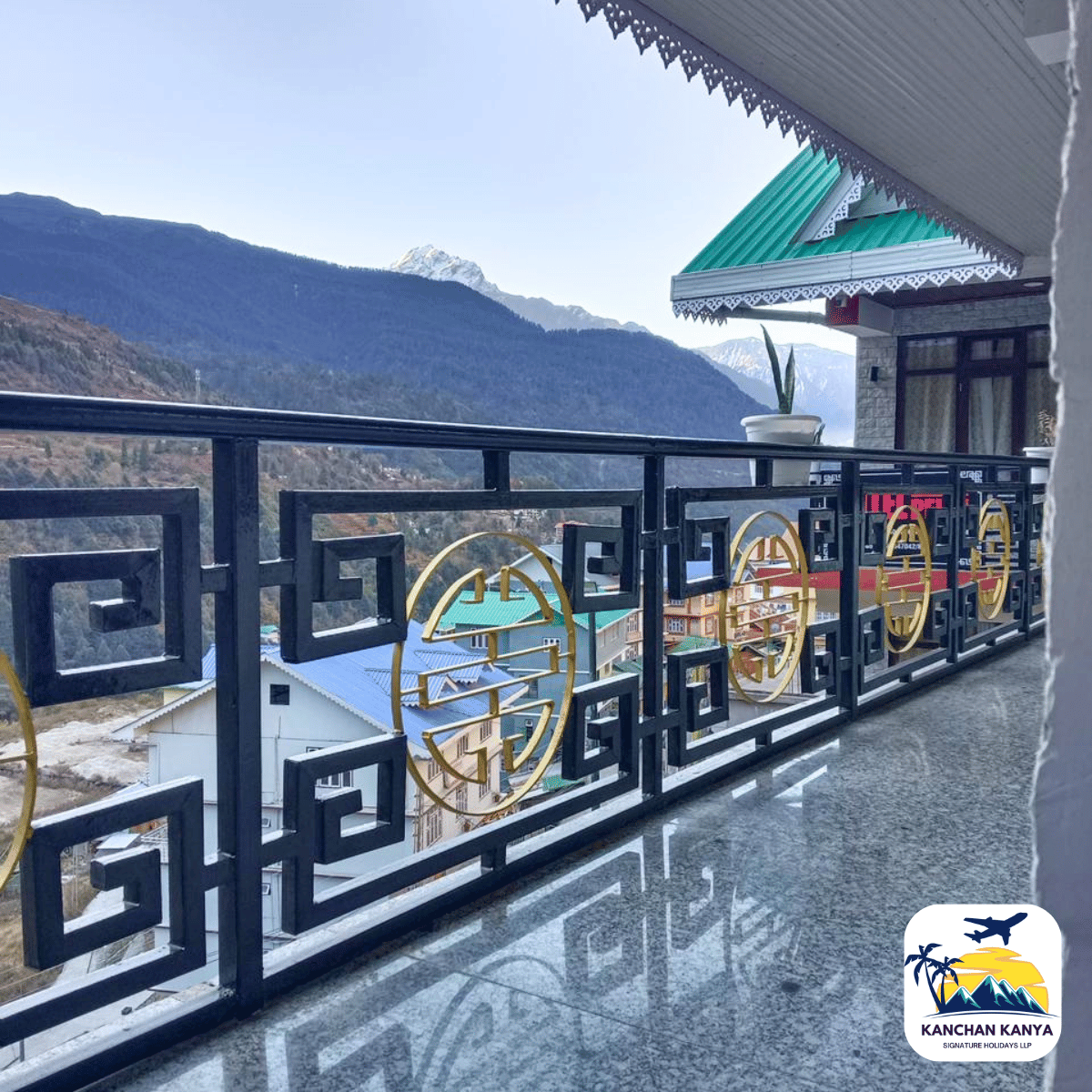 8 Balcony with a decorative black railing and gold circular motifs overlooks a mountain valley with rooftops below.