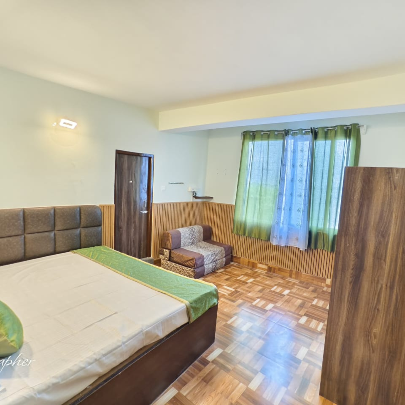 5 Hotel bedroom with a large bed and padded headboard, wooden wall panels, and green curtains by the window.
